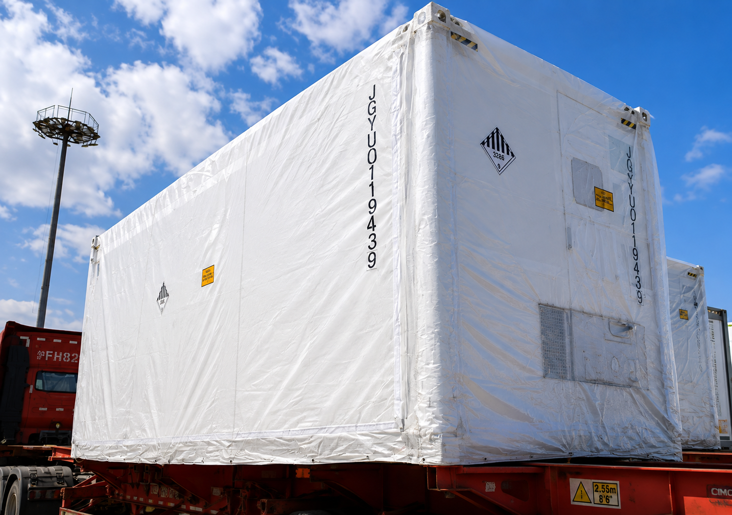 Weather-wrapped containerised BESS units loaded on trucks at the terminal, prepared for transport